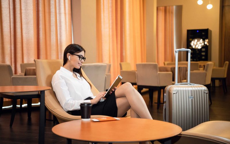 Femme d'affaires confiante écoutant de la musique sur sa tablette informatique, assise sur une chaise dans un salon d'affaires d'aéroport.