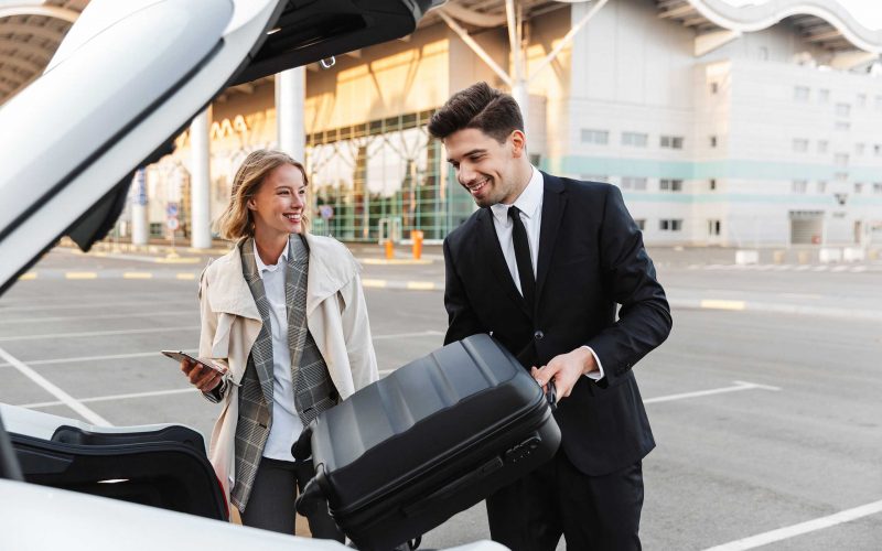 Image of young businesslike man and woman putting luggage in car